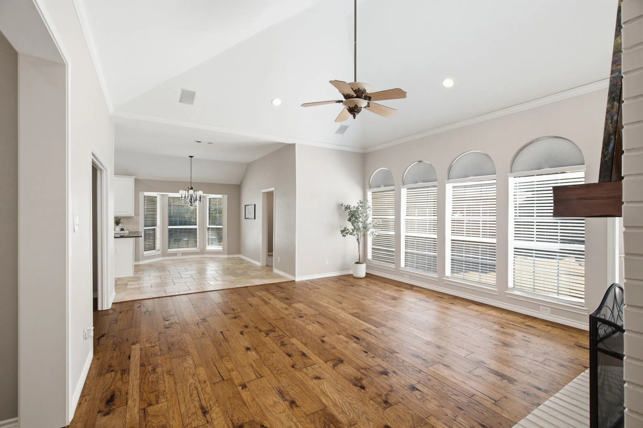 Spacious living area featuring vaulted ceilings, wood-finish flooring, a ceiling fan, recessed lighting, and a wall of arched windows with blinds