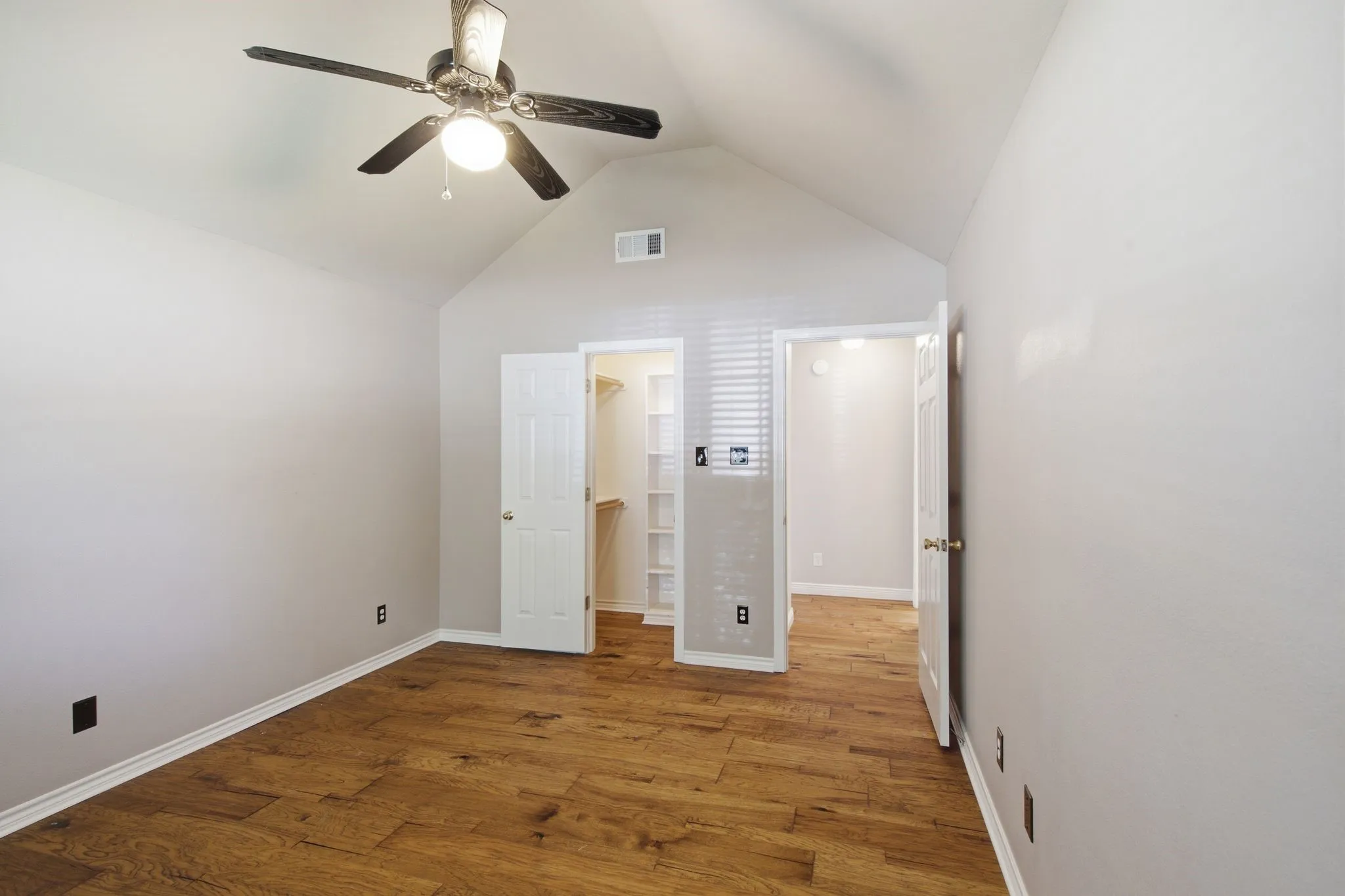 Vaulted ceilings with a ceiling fan light fixture, wood-finish flooring, white baseboards, and two doorways