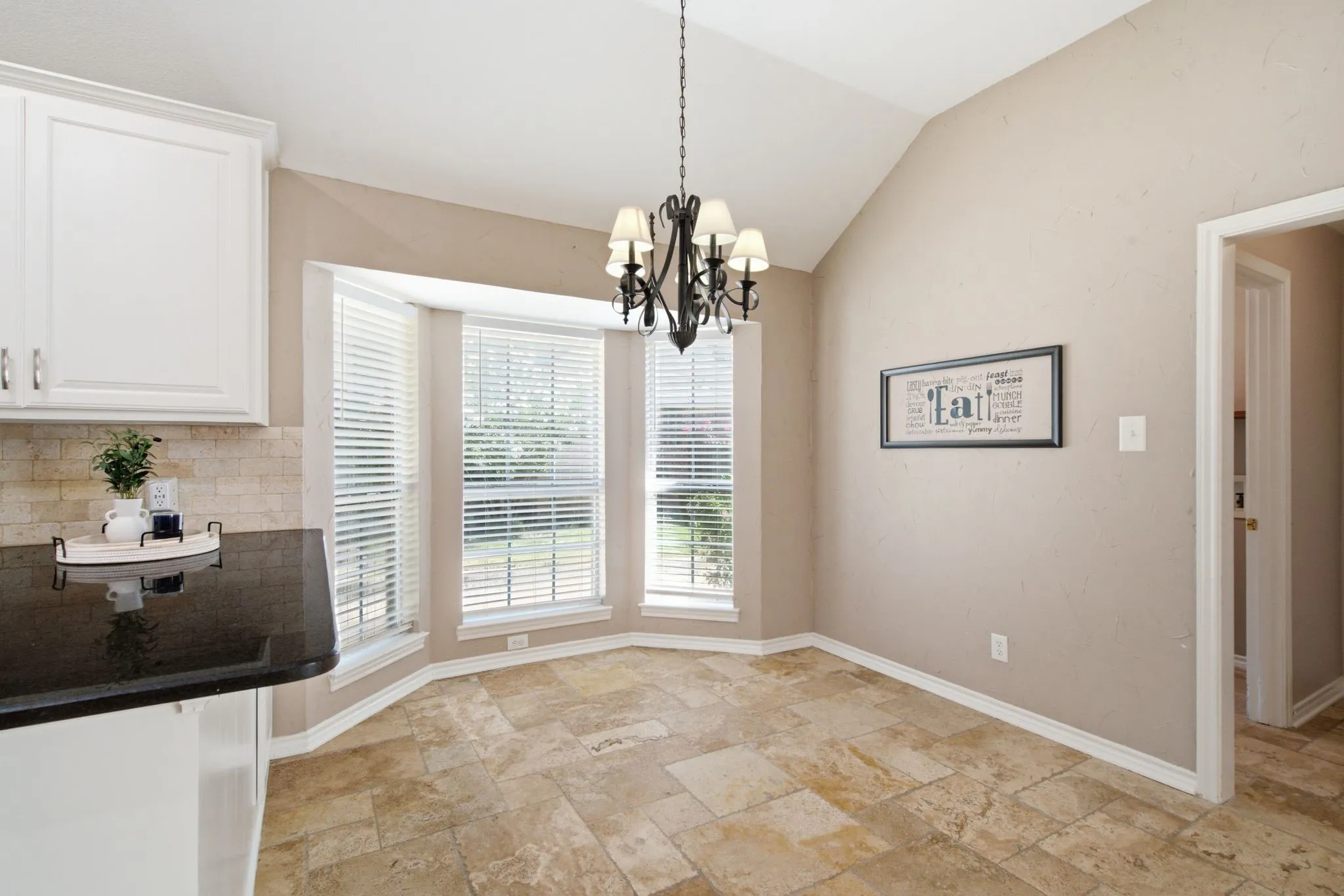 Vaulted ceiling with an iron chandelier, bay windows with blinds, and tile flooring
