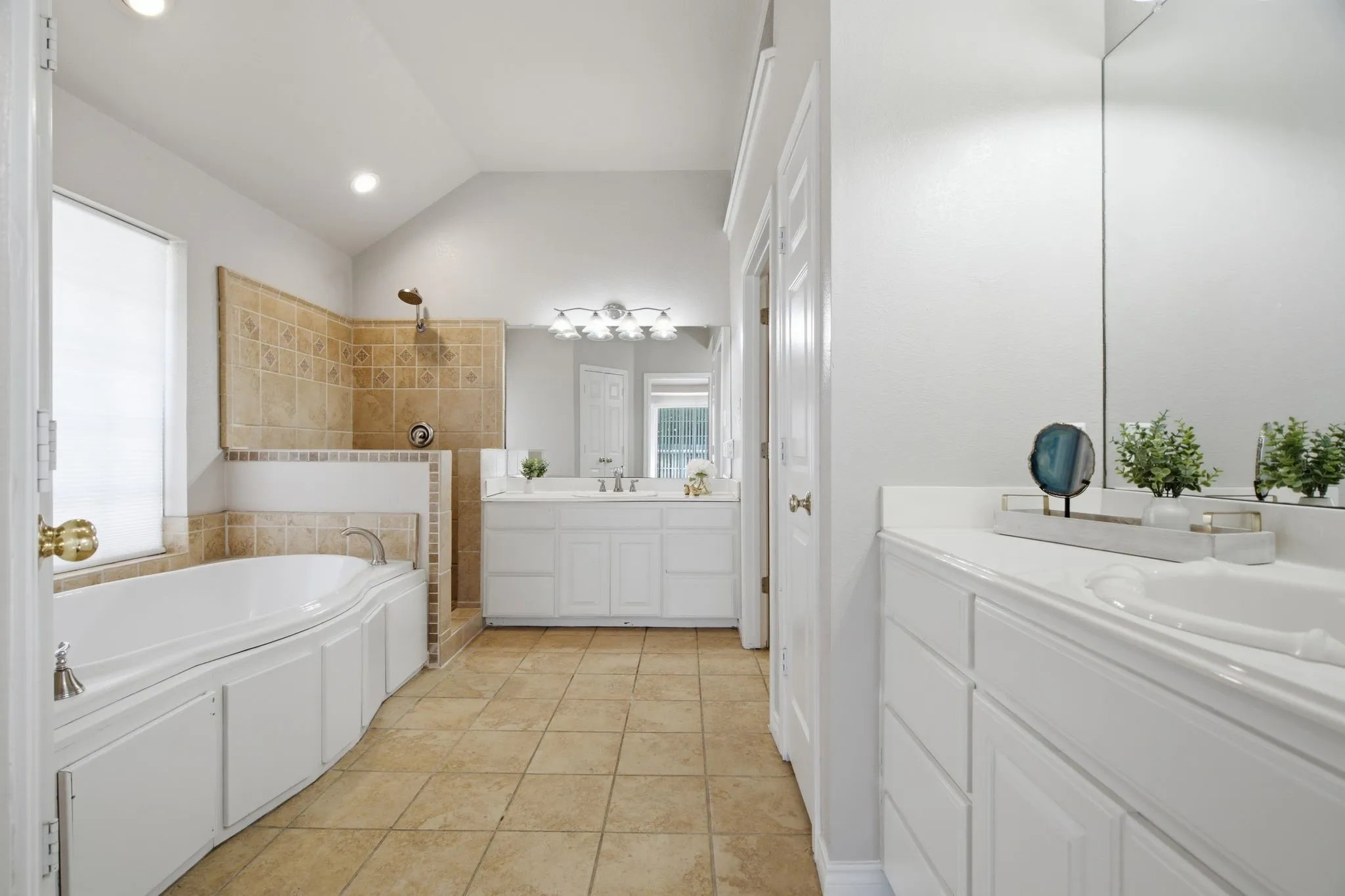 Light-filled bathroom featuring a soaking tub, separate tiled shower, and dual vanities with white cabinetry