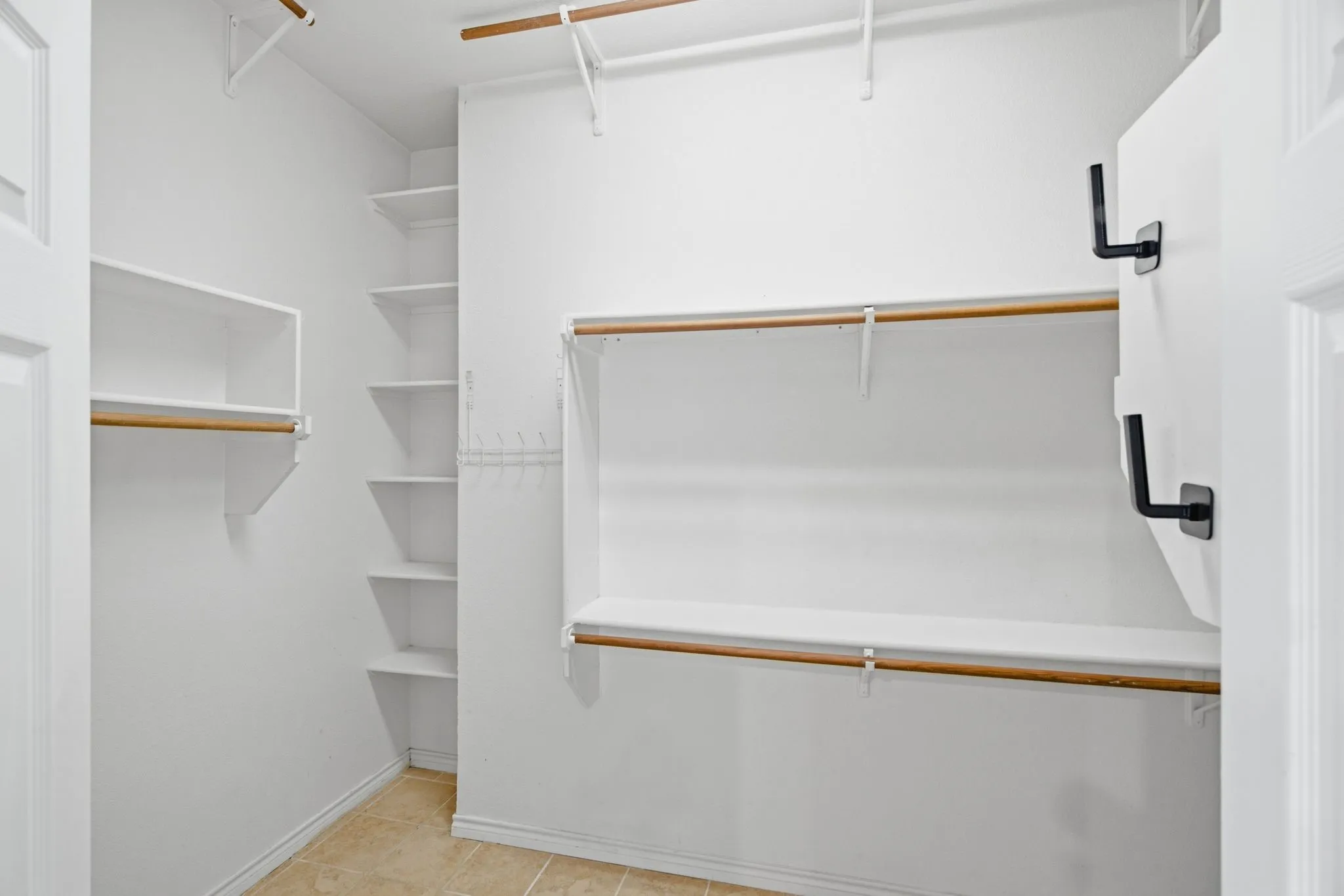 Expansive walk-in closet featuring multiple shelving units, garment rods, and light-toned tile flooring