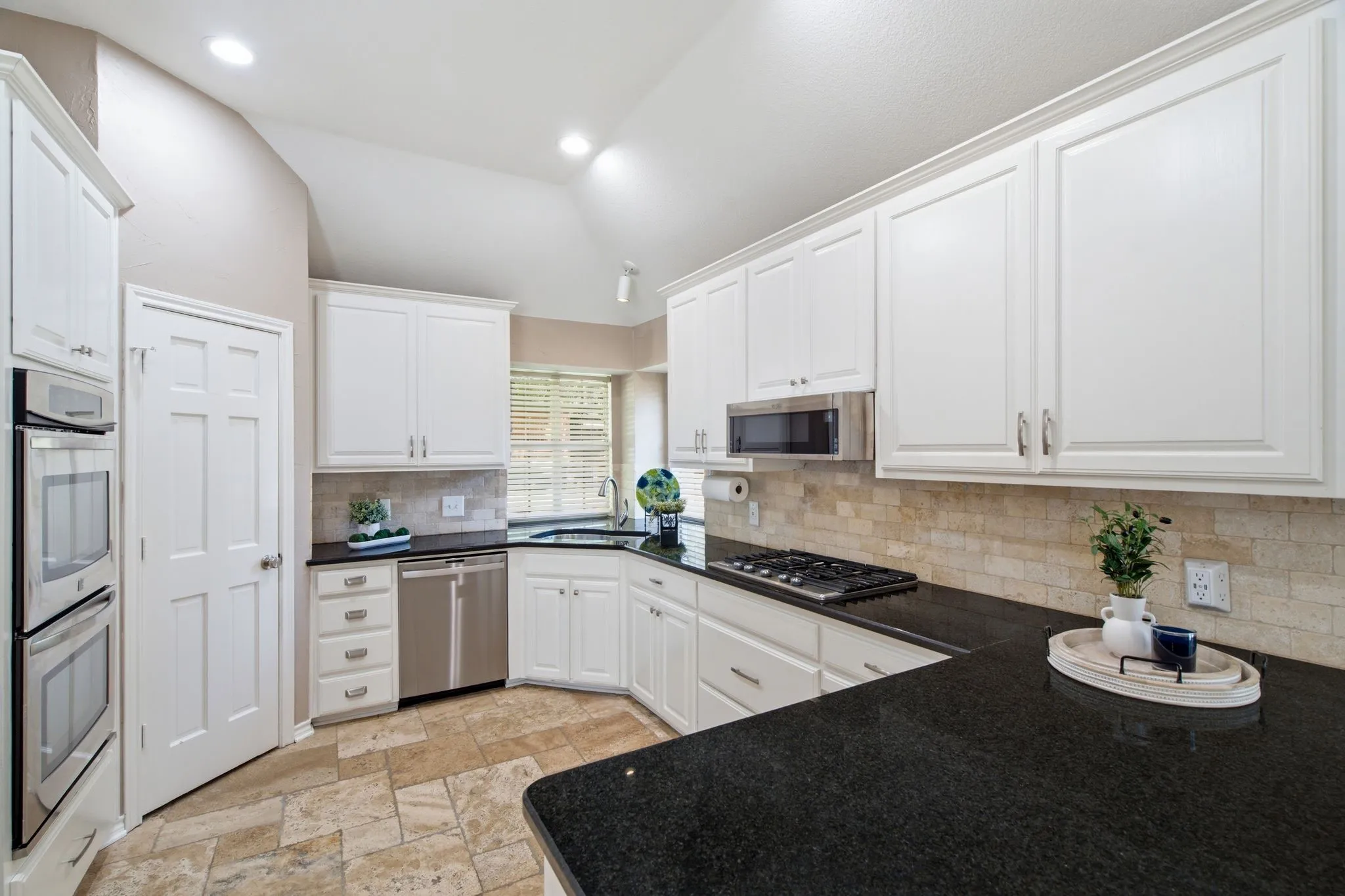 Kitchen featuring white cabinetry, black stone countertops, stainless steel appliances, a gas cooktop, and a stone tile backsplash