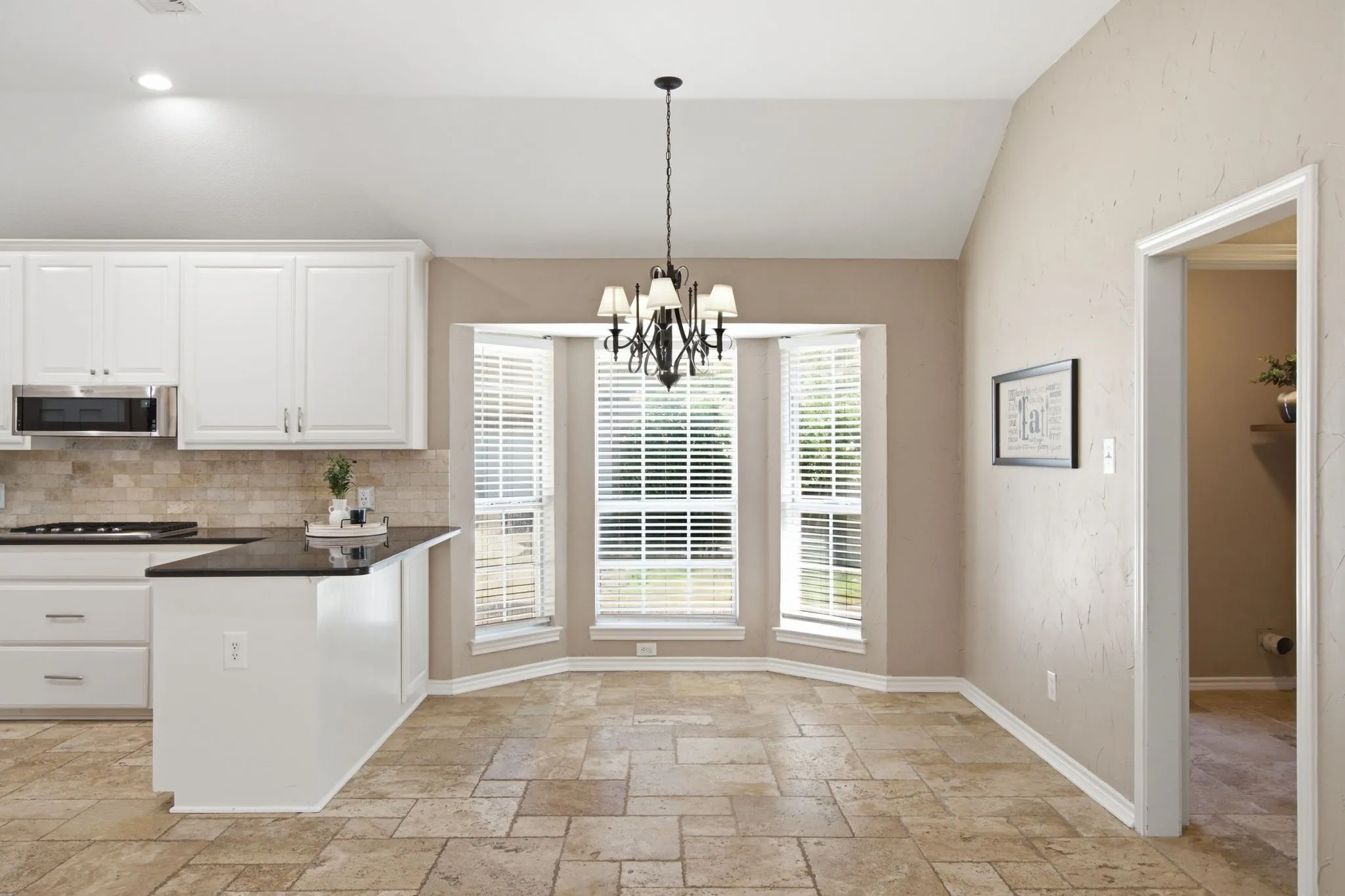 Kitchen and dining area featuring white cabinetry, black countertops, stainless steel microwave, stone tile backsplash, and a bay window