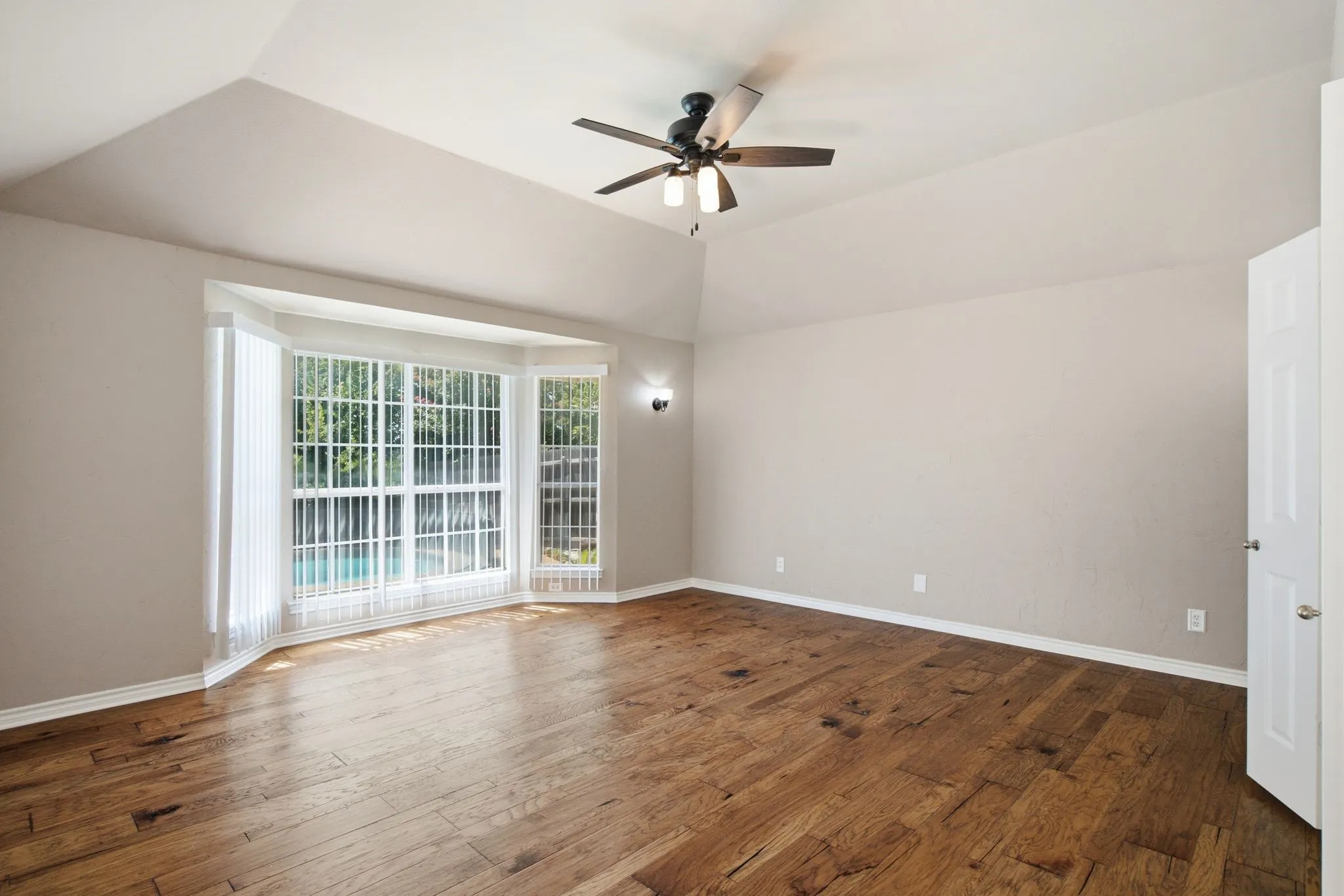 Spacious room featuring wood-finish flooring, a vaulted ceiling, and a prominent bay window overlooking a pool
