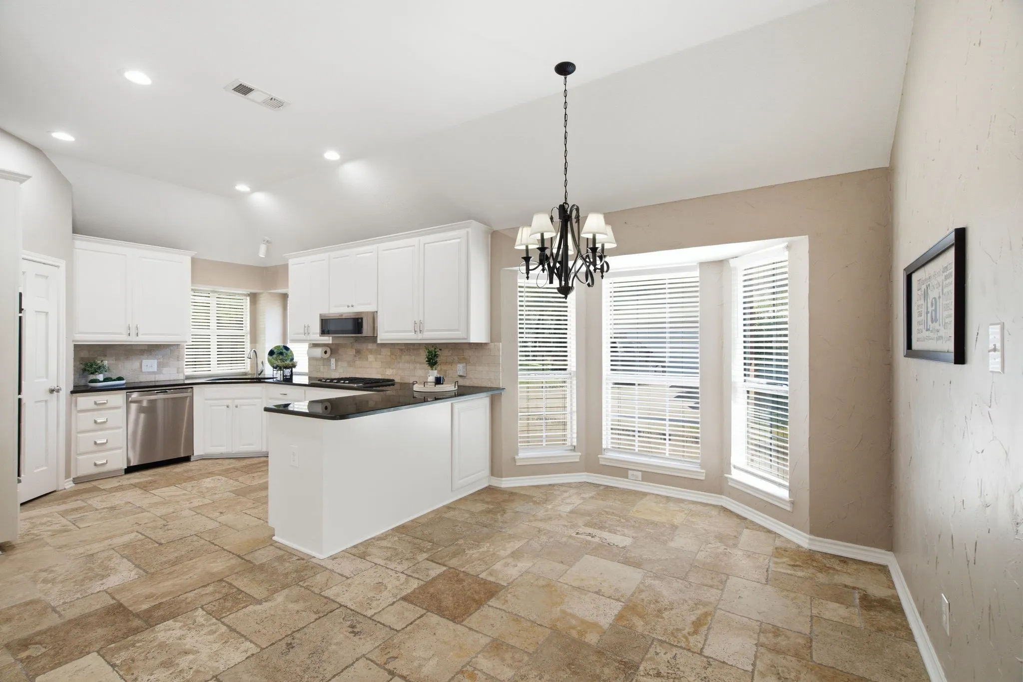Kitchen featuring white cabinetry, stainless steel appliances, a center island with dark countertops, and a bay window area with a decorative chandelier