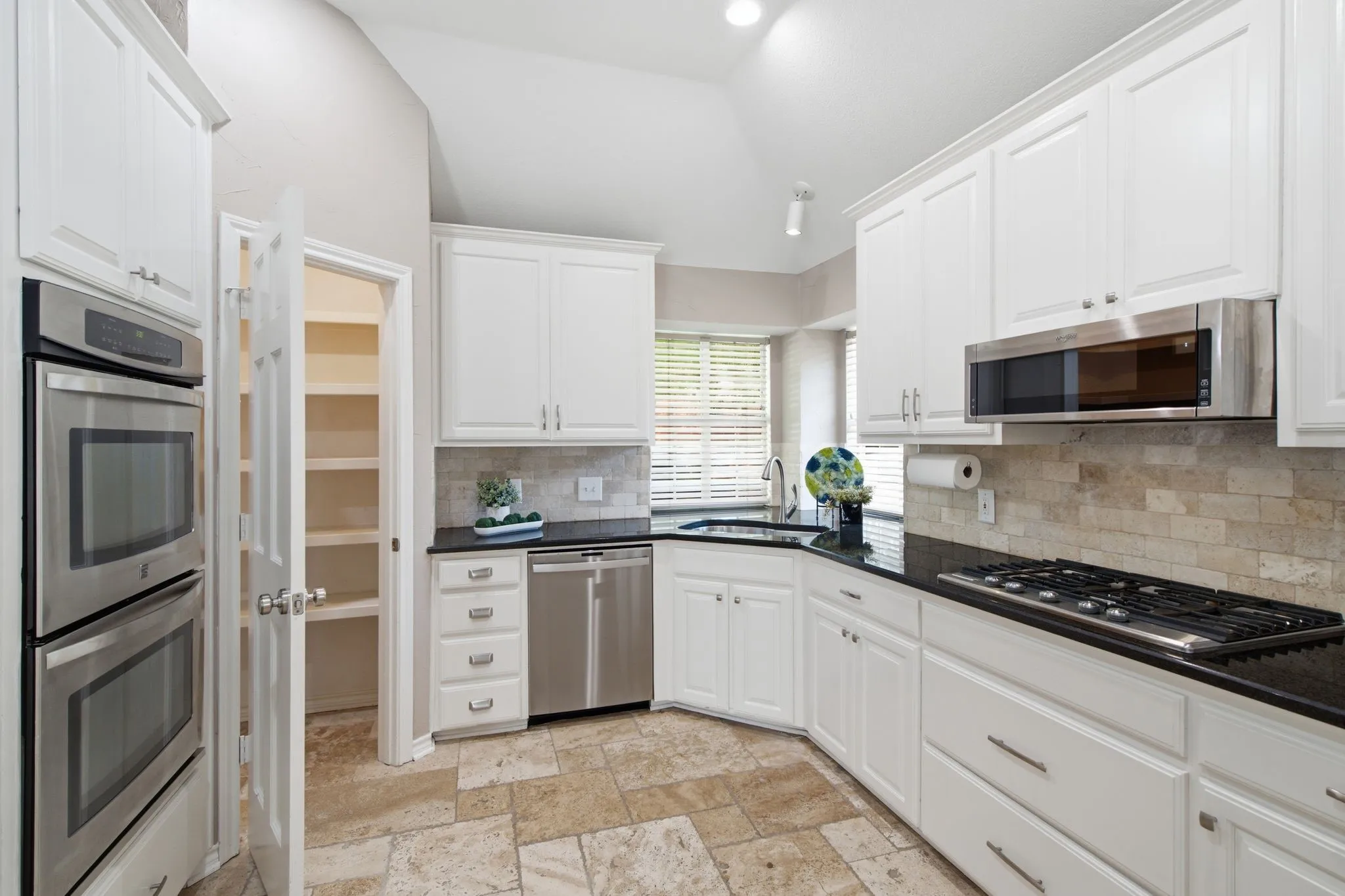 Kitchen featuring white cabinetry, black countertops, stainless steel appliances, a tile backsplash, and tile flooring