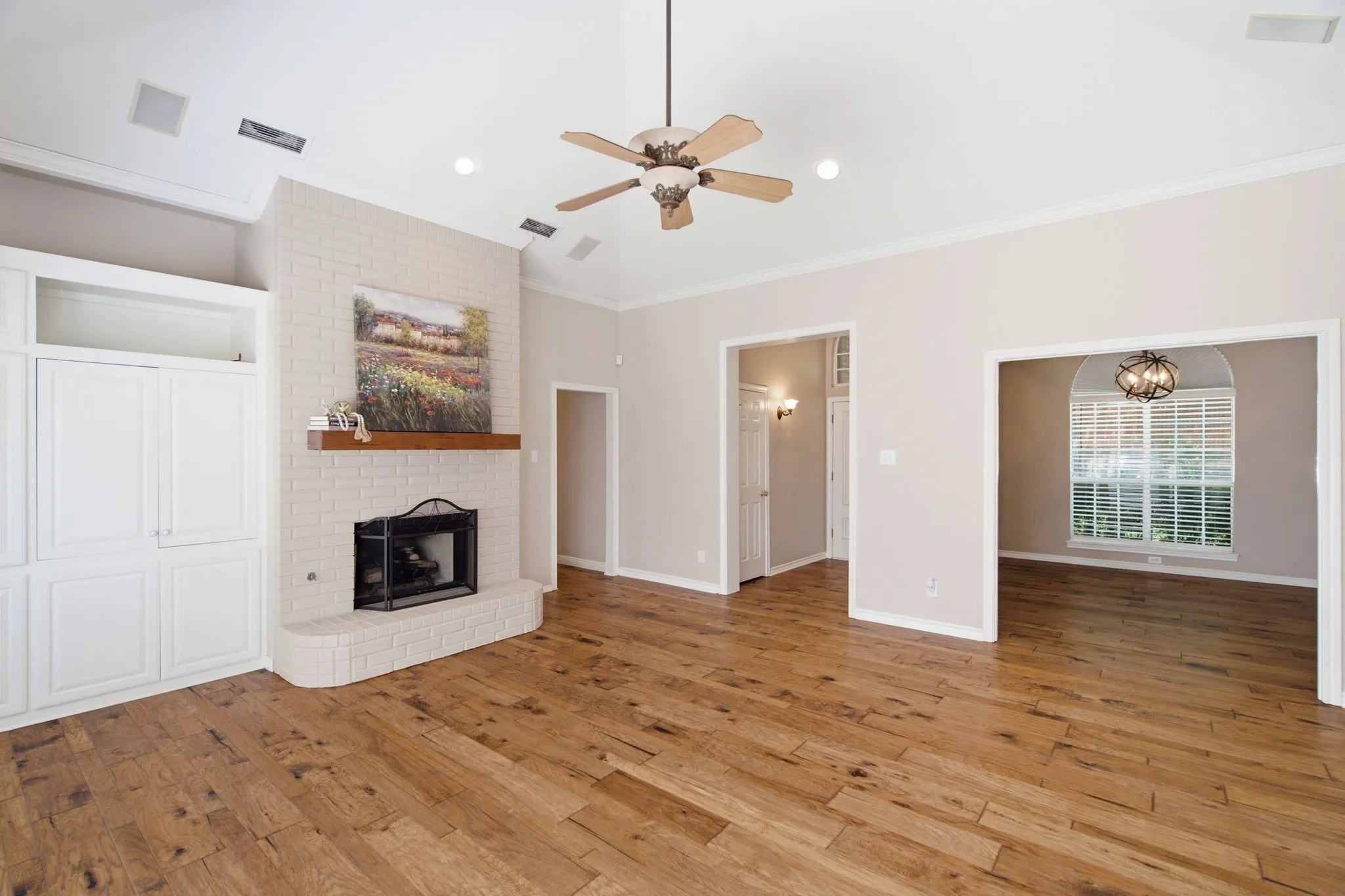 Spacious living area featuring high vaulted ceilings, wood-finish flooring, and a brick fireplace with a wood mantel