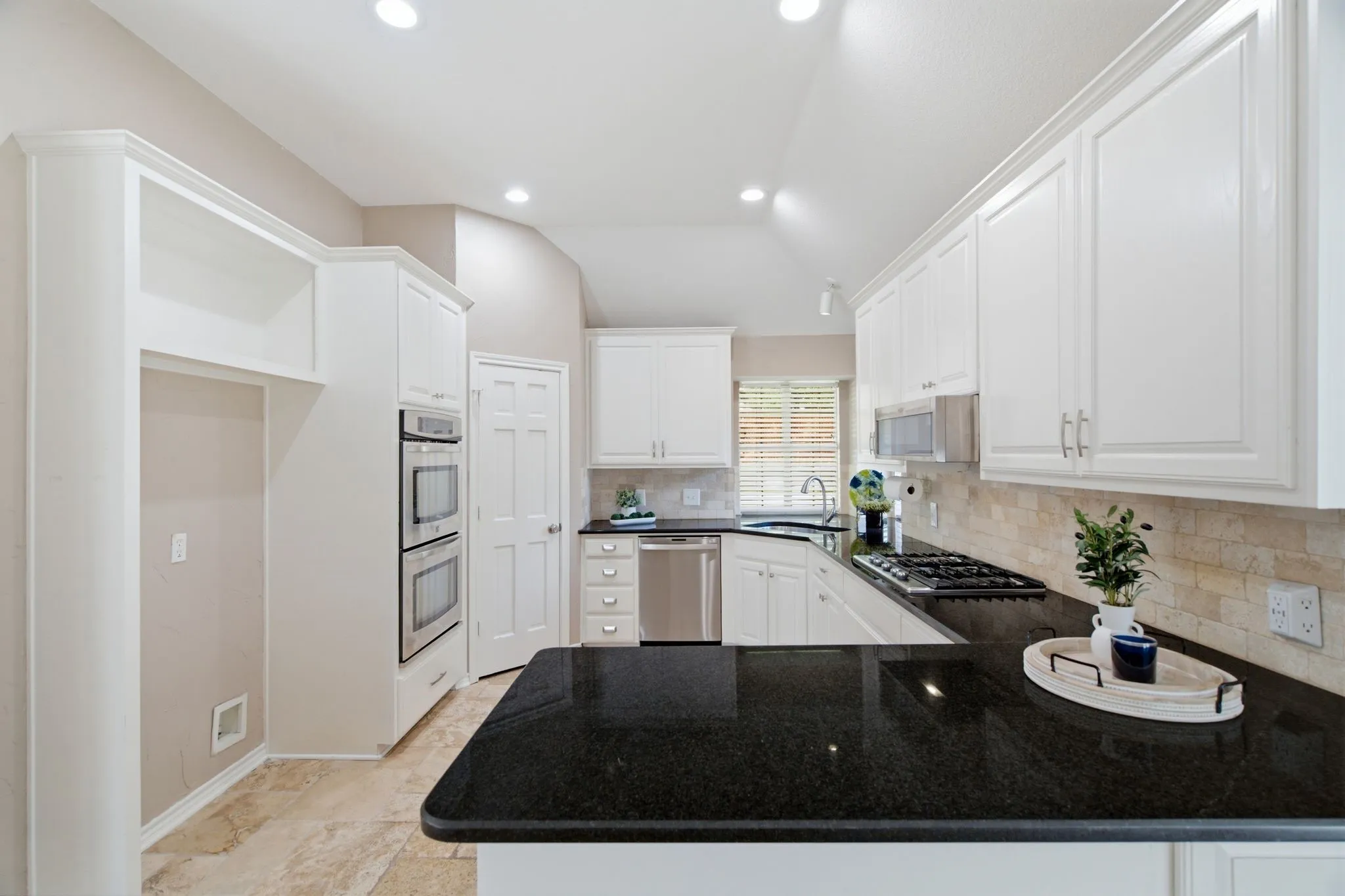 Kitchen with white cabinetry, black stone countertops, stainless steel double ovens, a gas cooktop, and beige tiled flooring