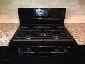 Black gas range with a digital display, flanked by speckled countertops and a light-toned subway tile backsplash