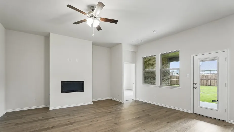 Spacious room featuring wood-finish flooring, a built-in fireplace, and a ceiling fan