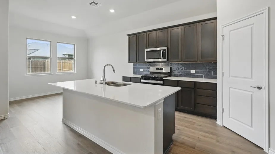 Kitchen featuring an expansive island with a stainless steel sink, dark wood-finish cabinetry, a stainless steel microwave, and wood-finish flooring