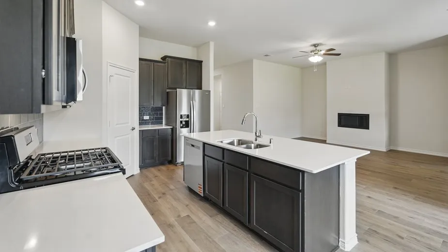 Open-concept kitchen featuring dark wood cabinetry, stainless steel appliances, a center island with double sinks, and light-toned countertops