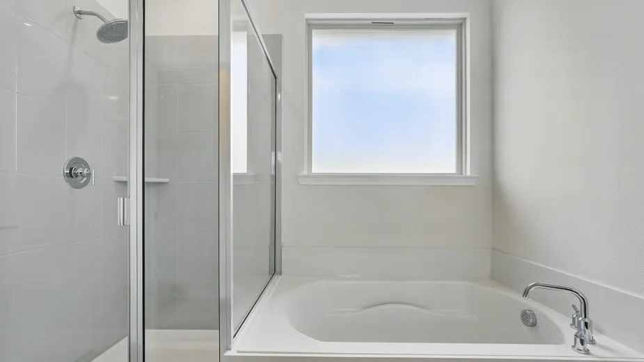 White soaking tub with chrome fixtures, framed by a frosted window