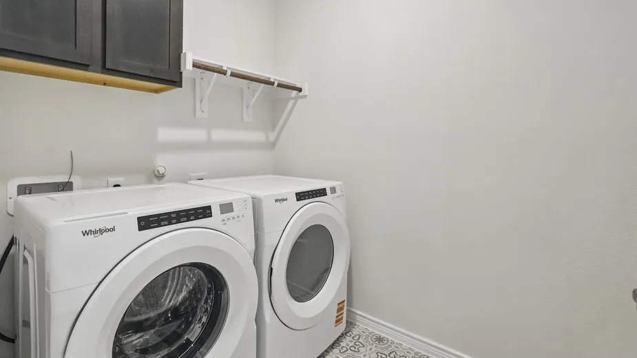 Dedicated laundry space featuring patterned floor tile, dark upper cabinetry, and a wall-mounted drying rack