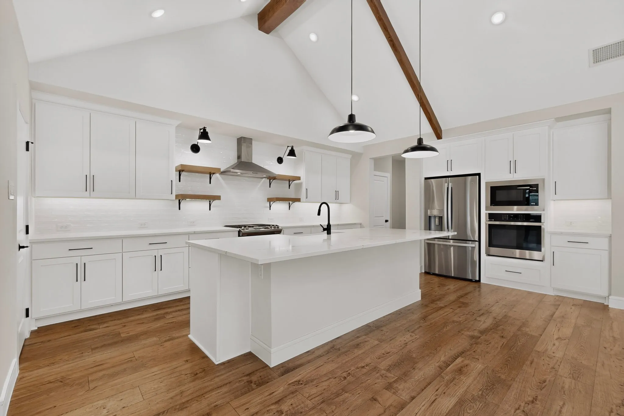 Vaulted ceilings with exposed wood beams, wood-finish flooring, white cabinetry, a kitchen island, and stainless steel appliances