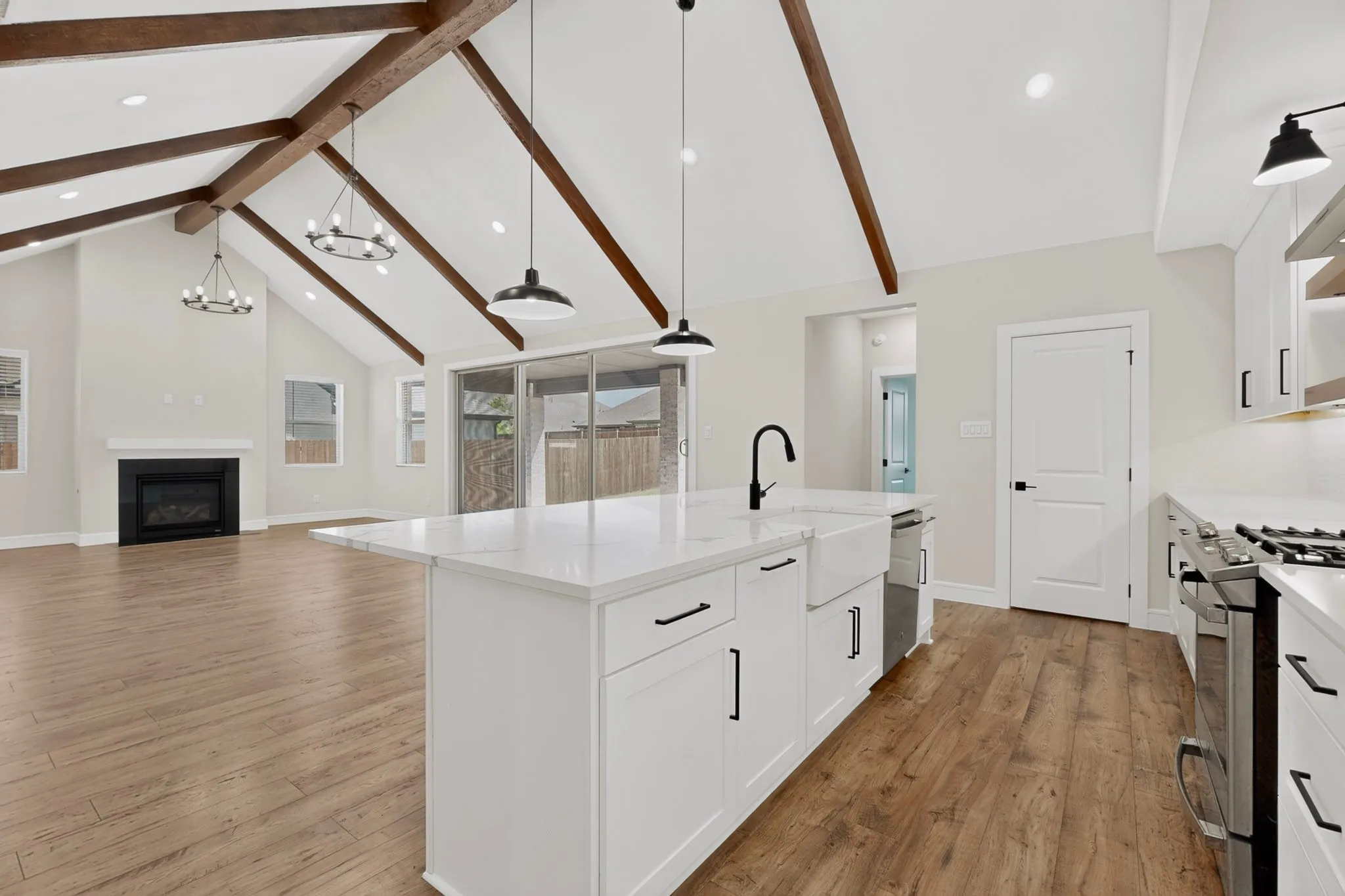 Vaulted ceilings with exposed wood beams, wood-finish flooring, white cabinetry, a kitchen island, and stainless steel appliances