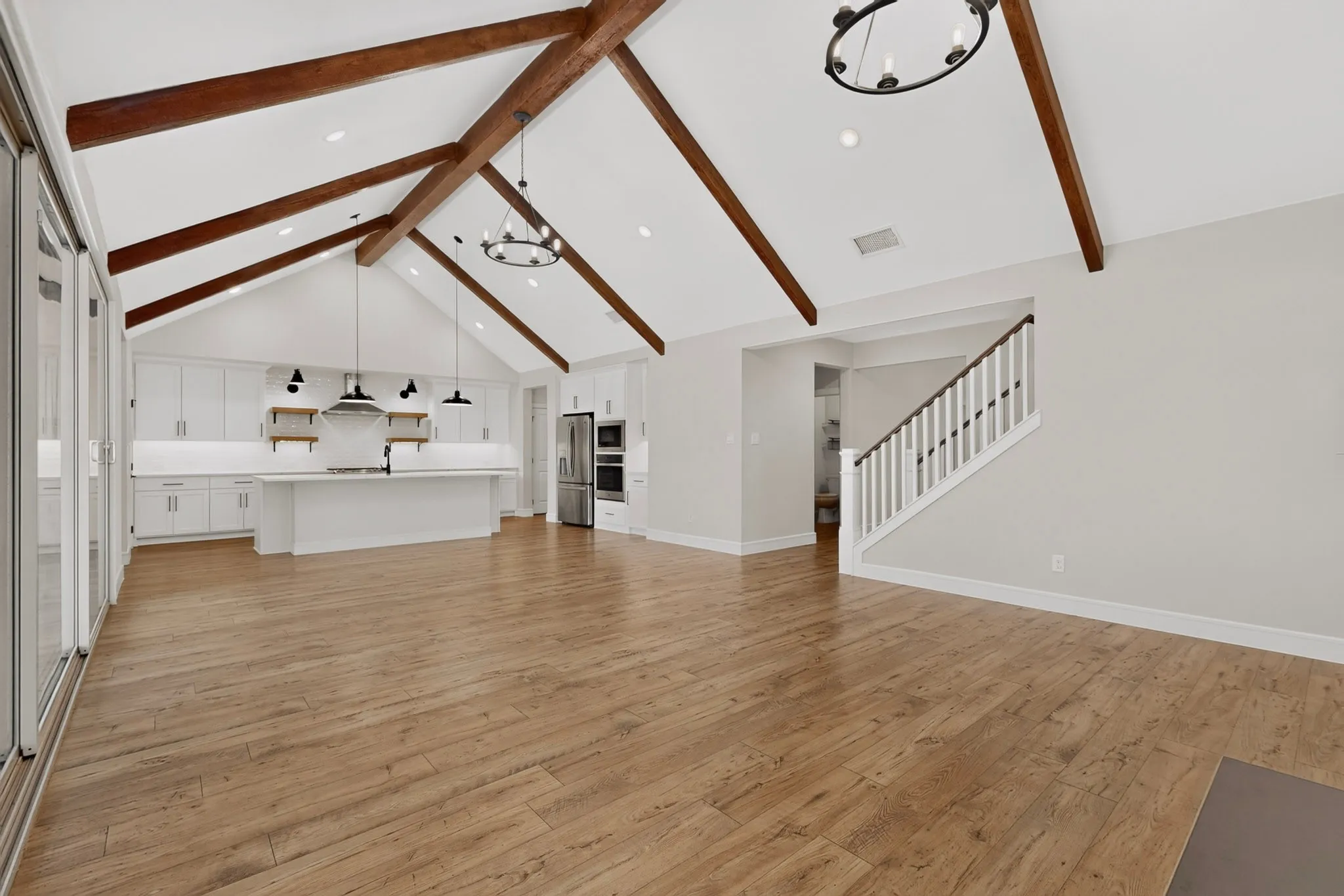 Vaulted ceilings with exposed wood beams, wood-finish flooring, white cabinetry, a kitchen island, and stainless steel appliances
