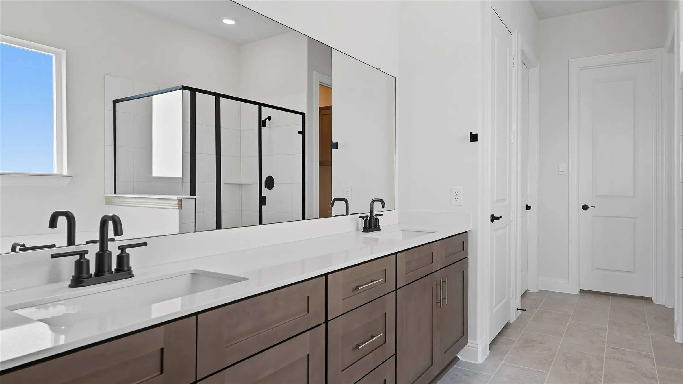 Bathroom featuring a dual vanity with dark wood-finish cabinetry, white countertop, and matte black fixtures