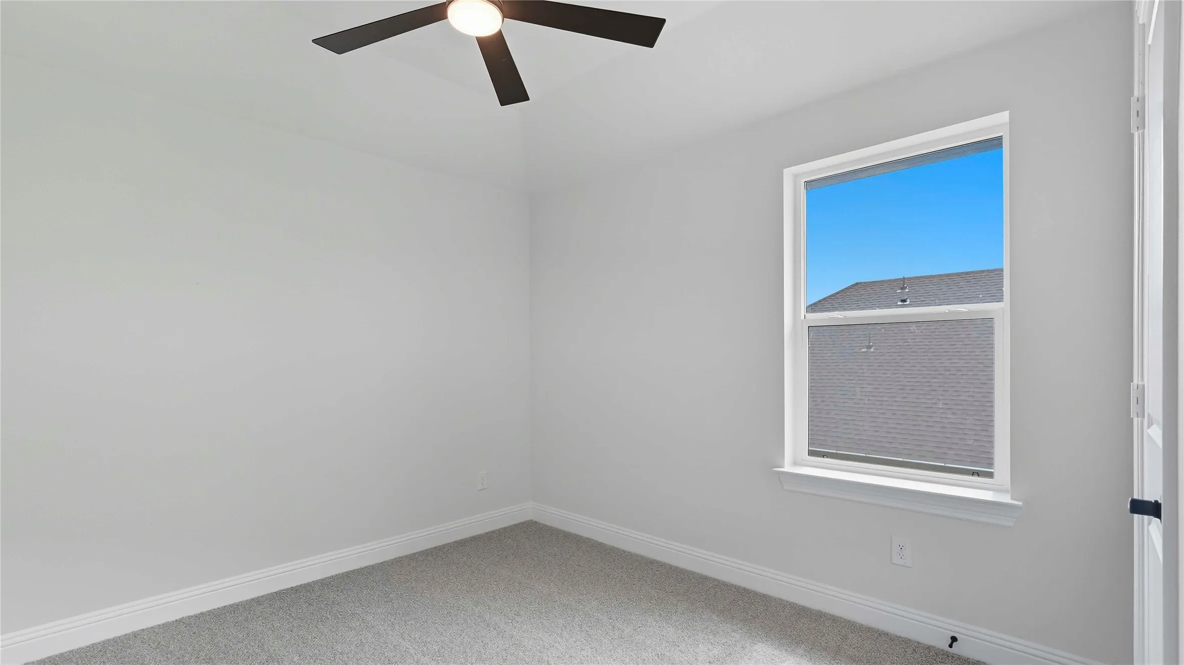 Bright interior space featuring a window with white trim, light gray carpet, white baseboards, and a ceiling fan with integrated lighting