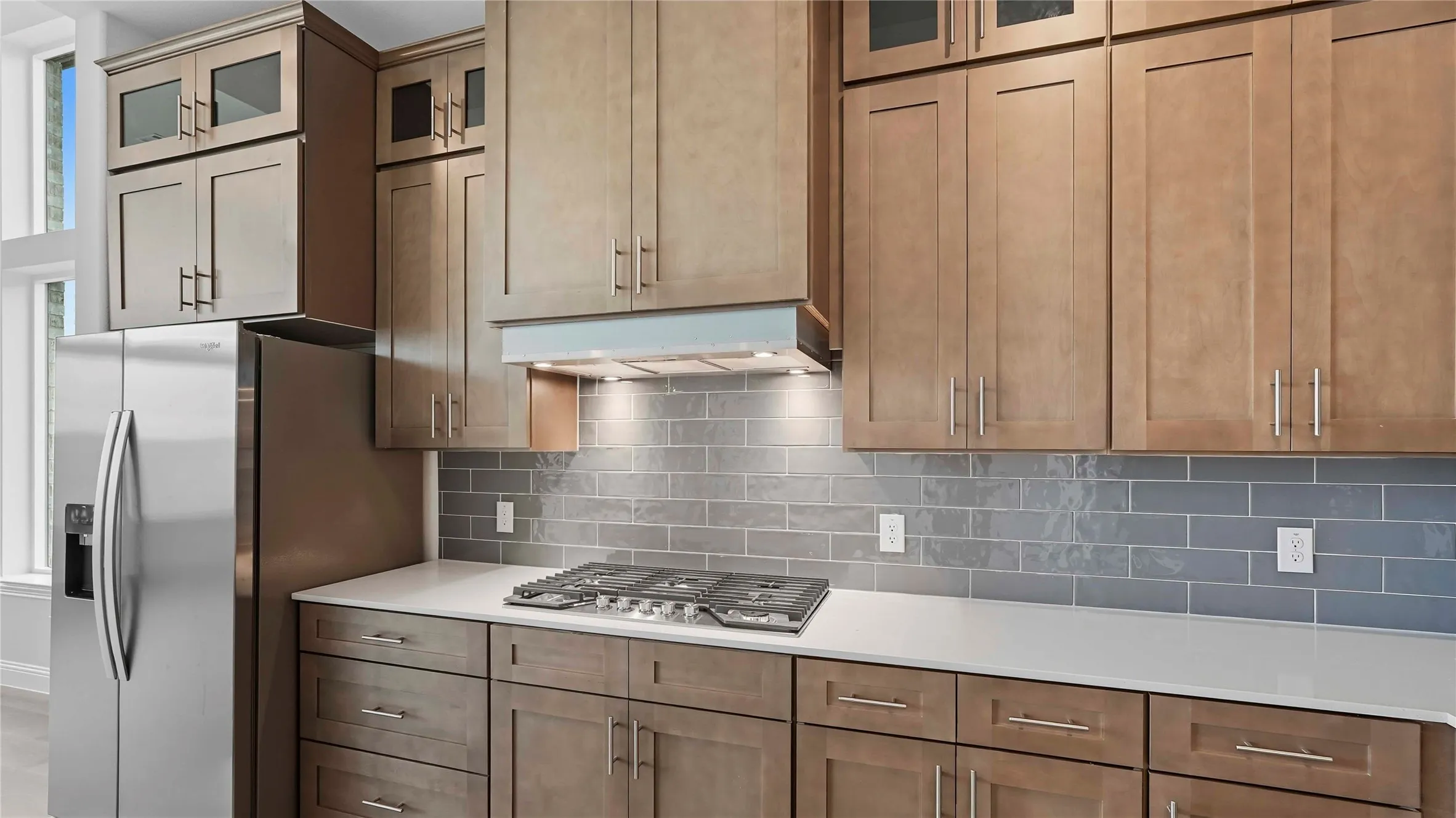 Modern kitchen featuring wood-finish cabinetry, stainless steel appliances, a subway tile backsplash, white countertops, and a gas cooktop
