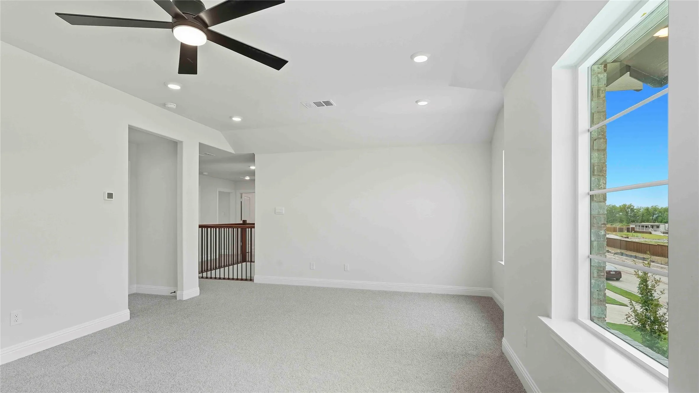 Expansive carpeted room featuring a ceiling fan with integrated lighting, recessed ceiling lights, and multiple windows