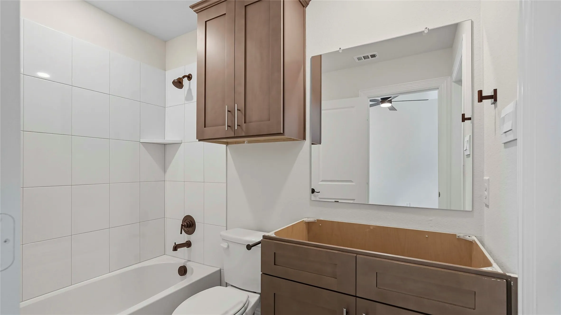 Bathroom featuring a white subway tile surround, dark bronze fixtures, built-in shelving, and a vanity cabinet base with matching overhead storage