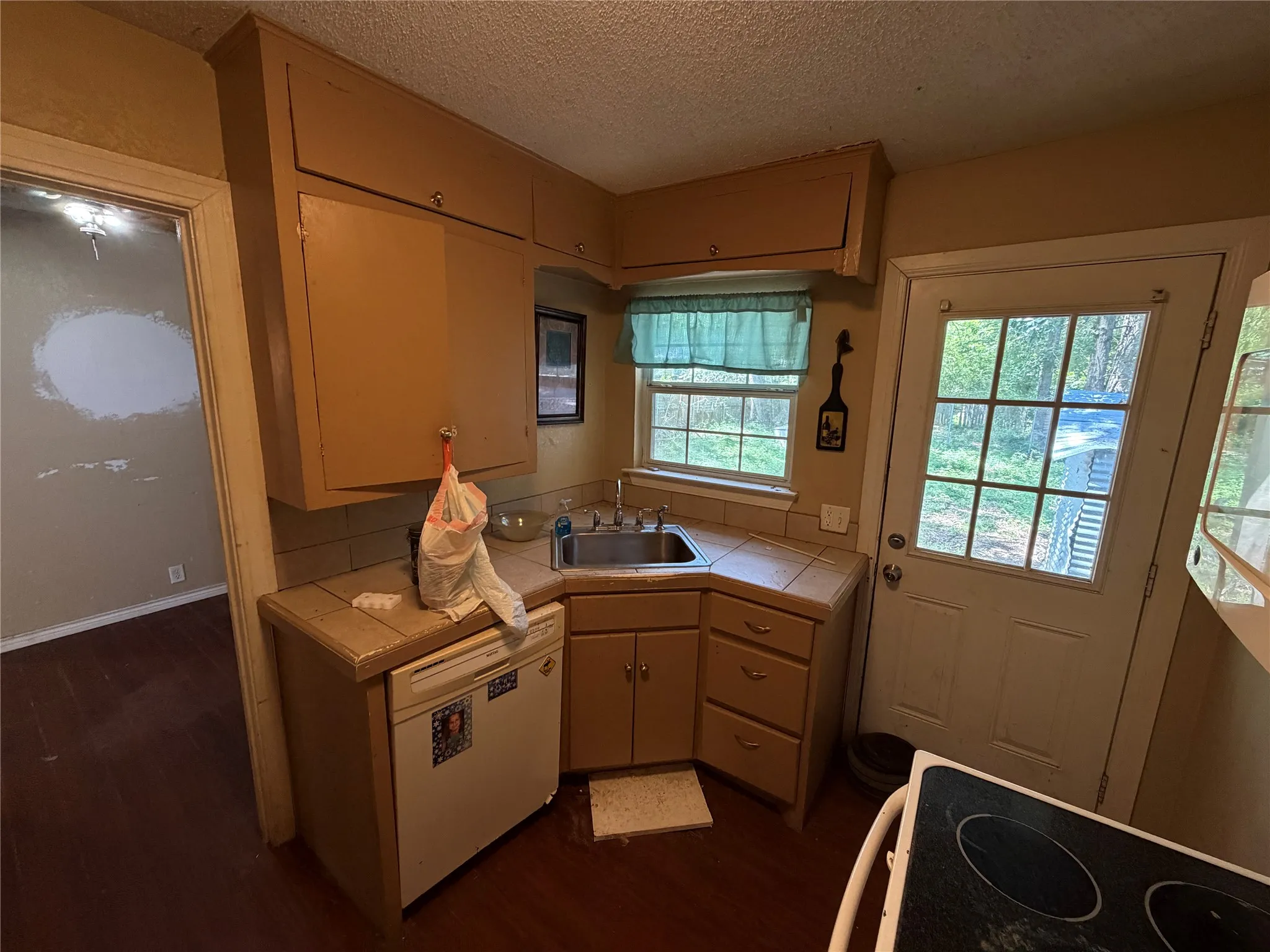 Compact kitchen featuring wood-finish flooring, a stainless steel sink, tiled countertops, and ample upper and lower cabinetry
