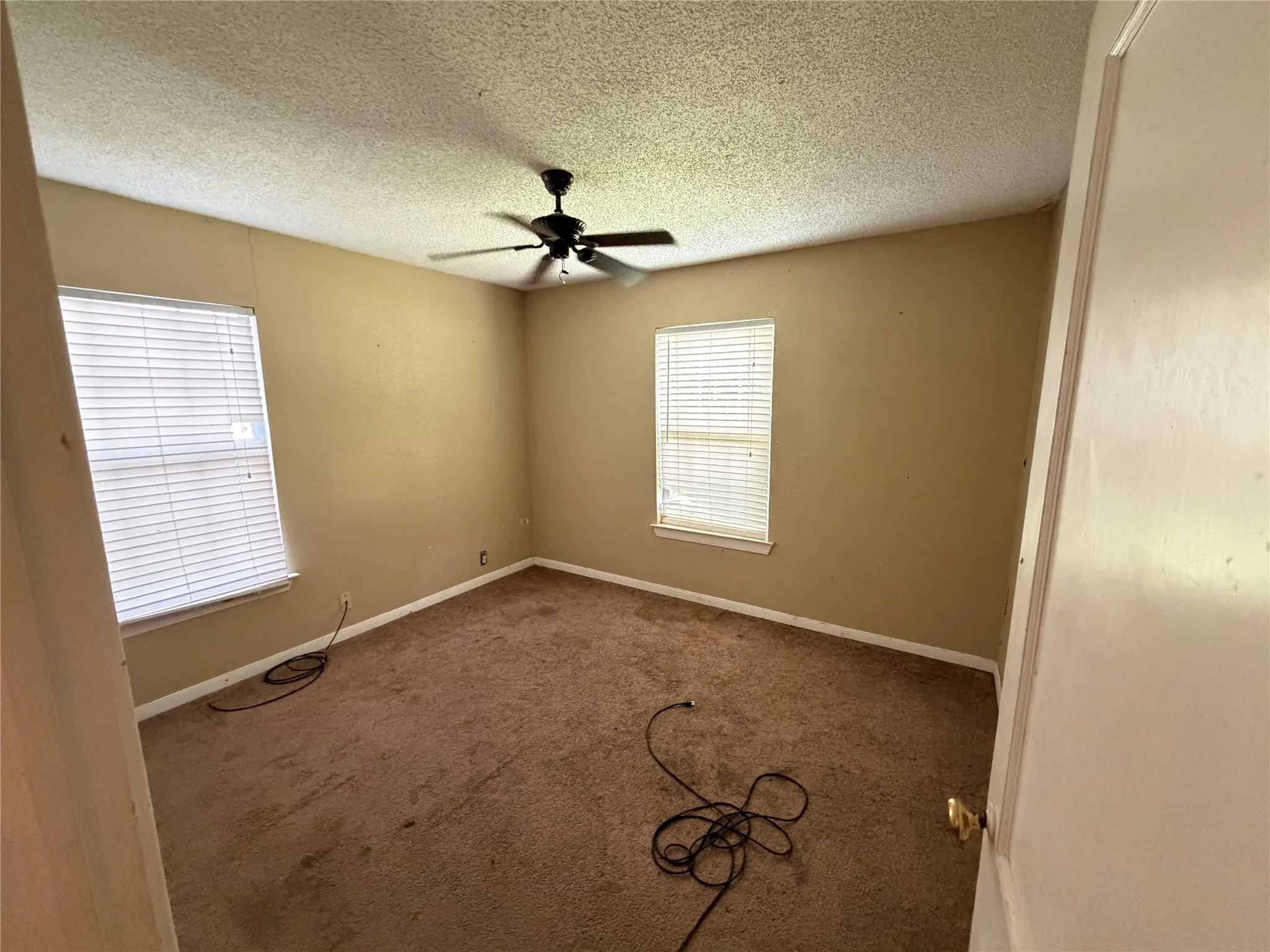 Room featuring neutral wall tones, textured ceiling, brown carpeting, and two windows with horizontal blinds