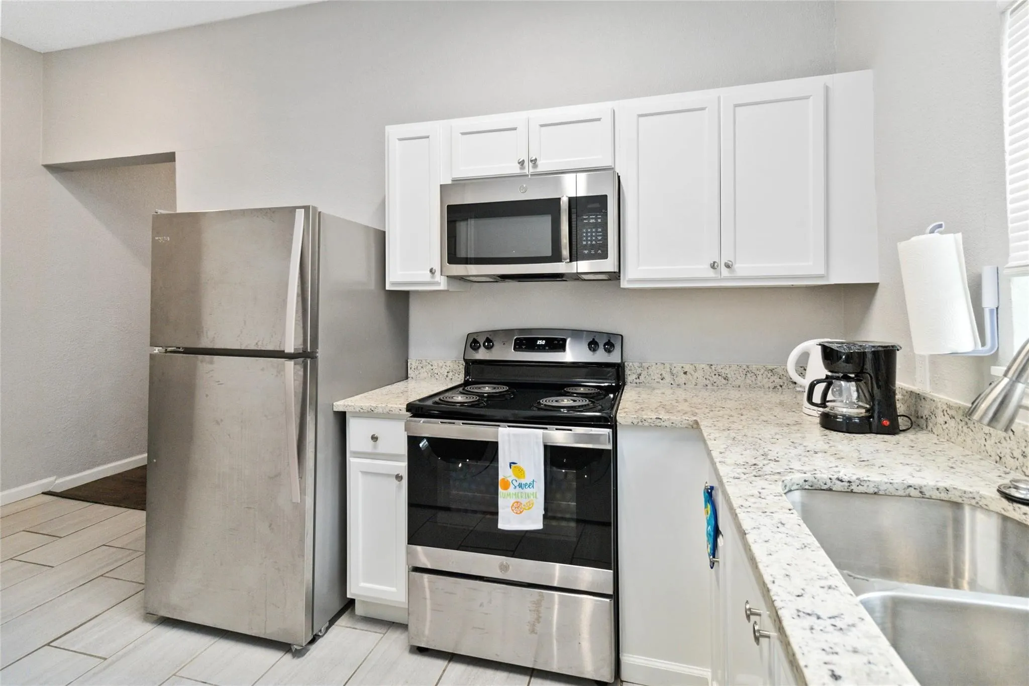Kitchen with a sink, white cabinetry, baseboards, appliances with stainless steel finishes, and light stone countertops