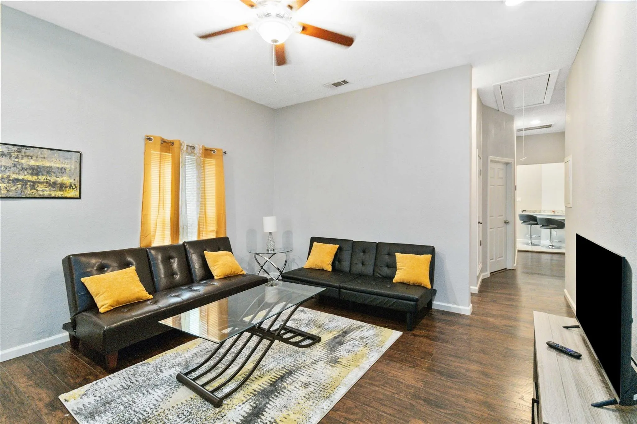 Living room with attic access, visible vents, baseboards, a ceiling fan, and dark wood-style floors