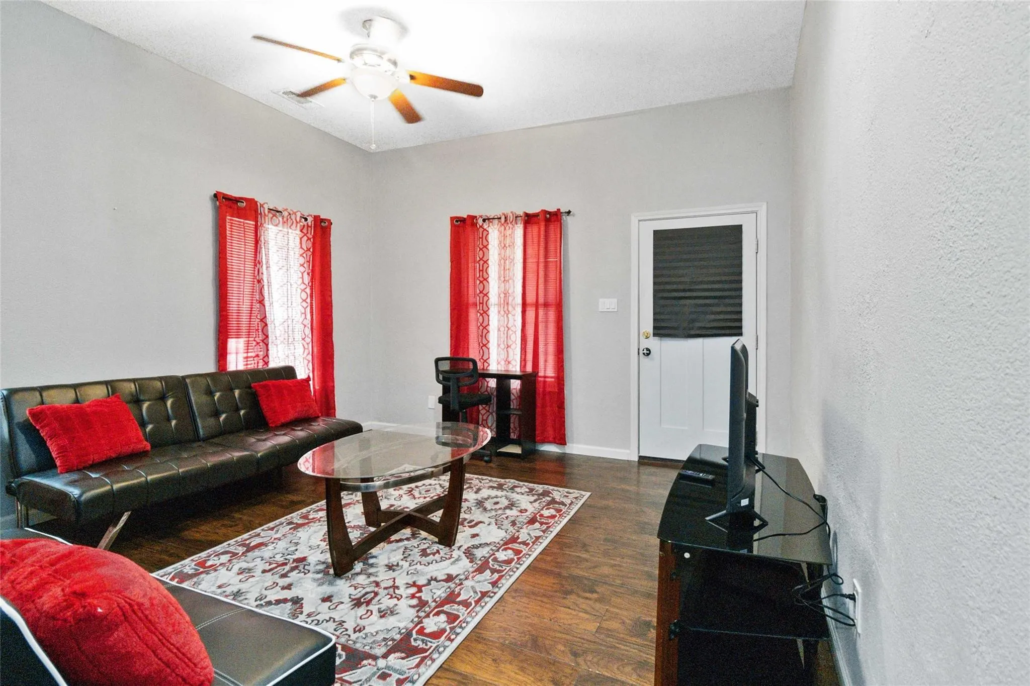 Living area featuring ceiling fan, baseboards, dark wood finished floors, and a textured wall
