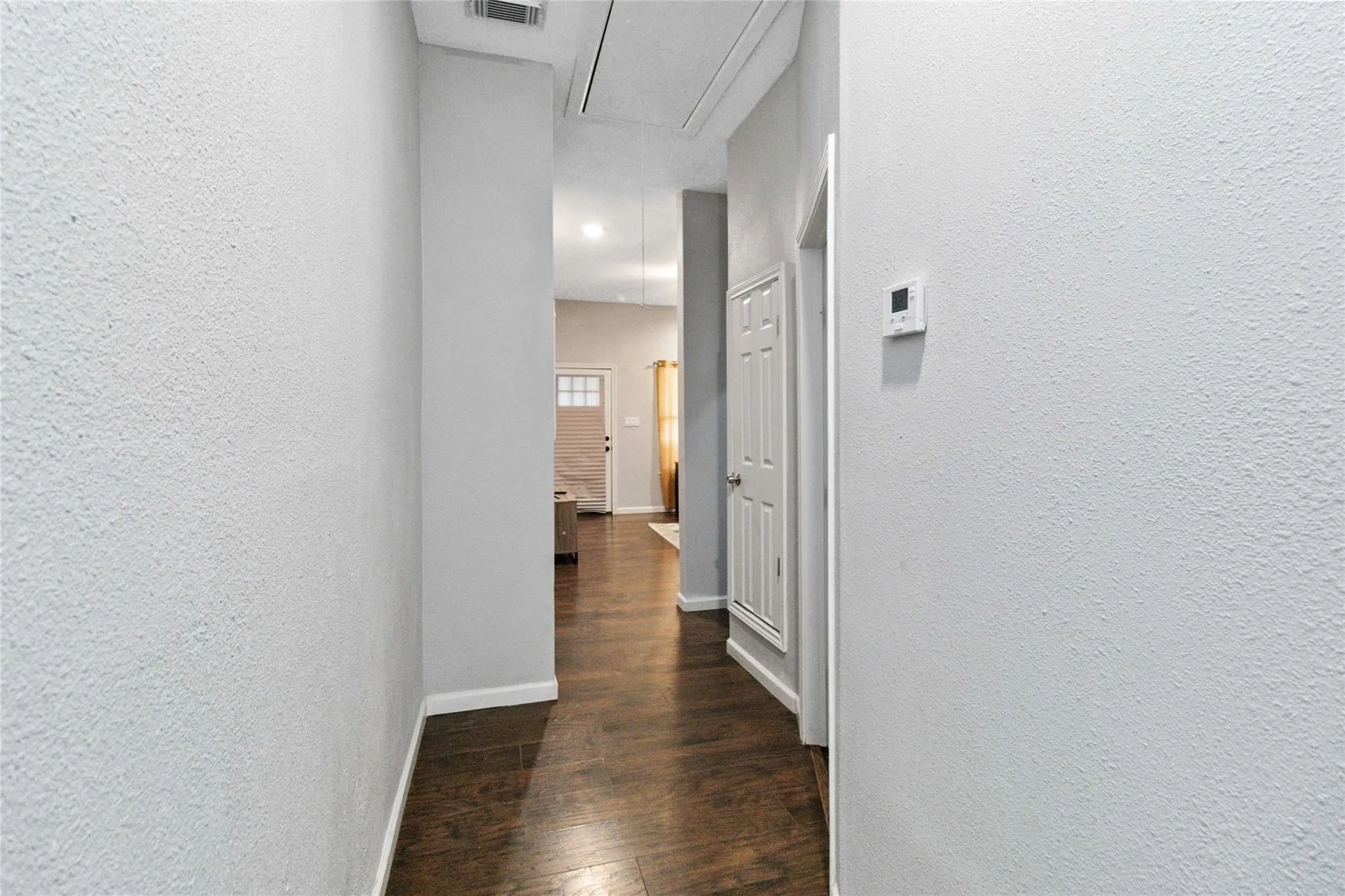 Hall with attic access, visible vents, baseboards, dark wood finished floors, and a textured wall