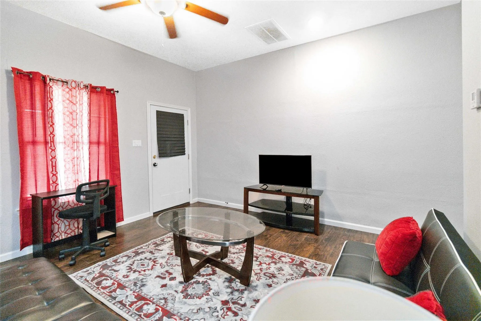 Living area featuring dark wood-style floors, baseboards, visible vents, and a ceiling fan