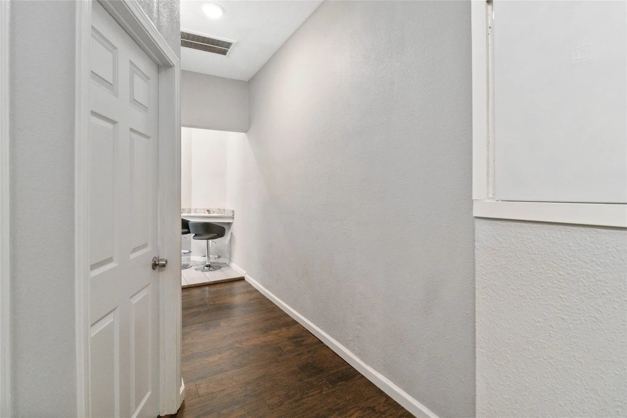Corridor with dark wood-type flooring, visible vents, a textured wall, and baseboards