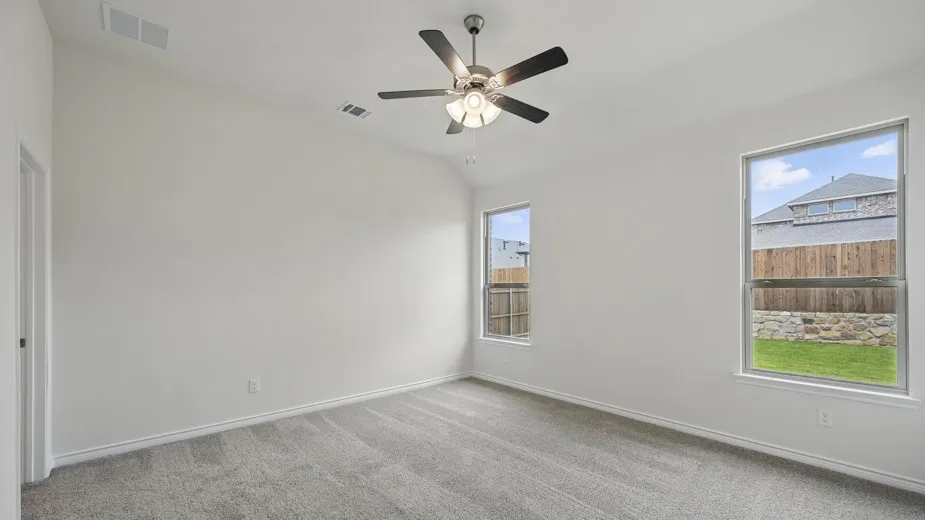 Spacious room featuring neutral carpeting, white walls, two windows, and a ceiling fan with integrated lighting