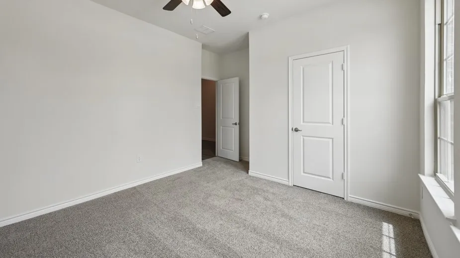 Spacious room featuring light gray carpeting, white painted walls, and a ceiling fan with integrated lighting