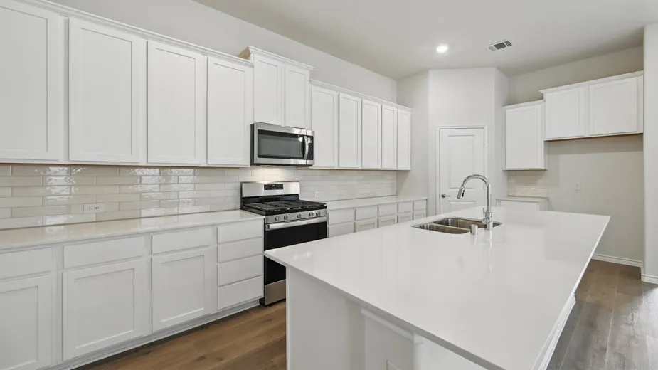 Kitchen featuring a central island with a double basin sink, white cabinetry with crown molding, white subway tile backsplash, stainless steel microwave, and a stainless steel gas range