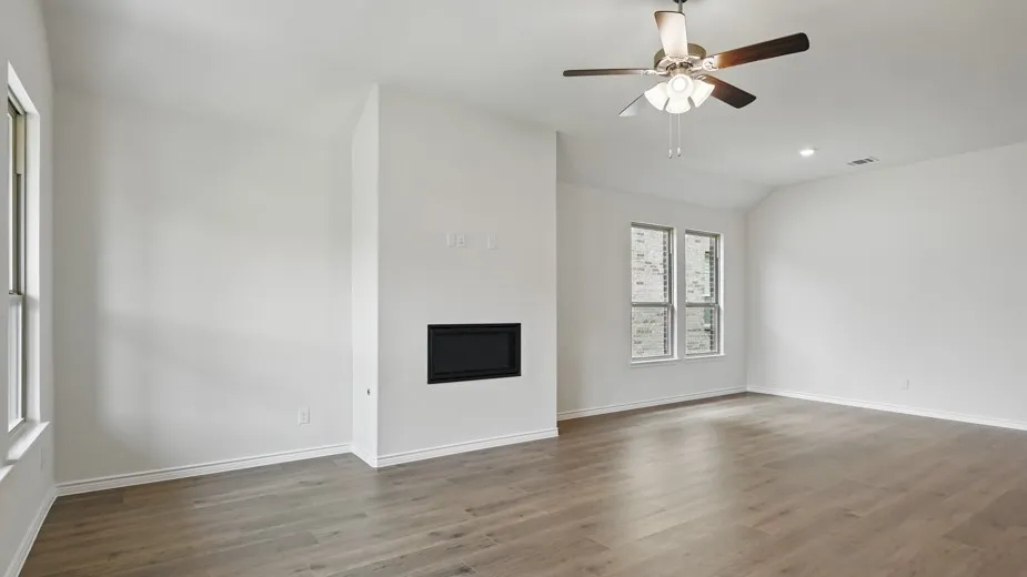 Spacious room featuring wood-finish flooring, an integrated fireplace, and multiple windows