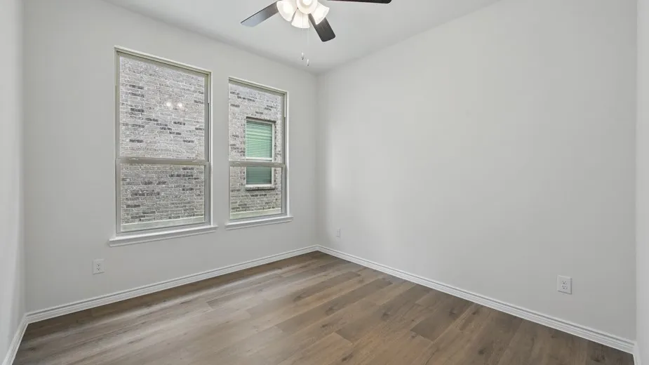 Bright room featuring two large windows with white trim, wood-finish flooring, and a ceiling fan with integrated lighting