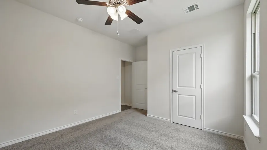 Carpeted room featuring a ceiling fan with light fixture, white walls, white trim, and a window providing natural illumination