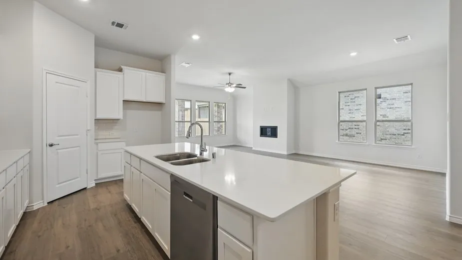 Expansive kitchen island featuring a double basin sink, stainless steel dishwasher, and light-toned solid surface countertop