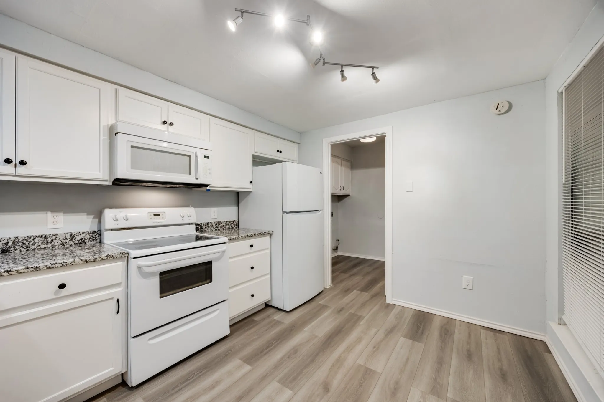 Kitchen featuring white cabinetry, granite-patterned countertops, wood-finish flooring, white appliances, and track lighting