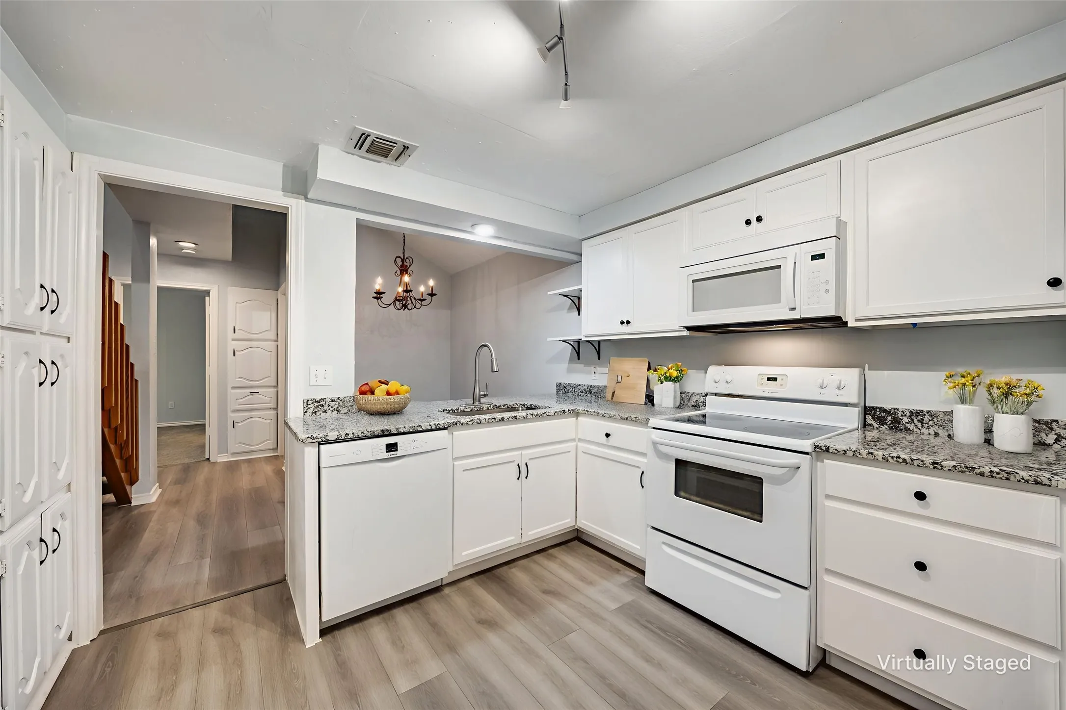White kitchen cabinetry with black hardware, granite-style countertops, and wood-finish flooring