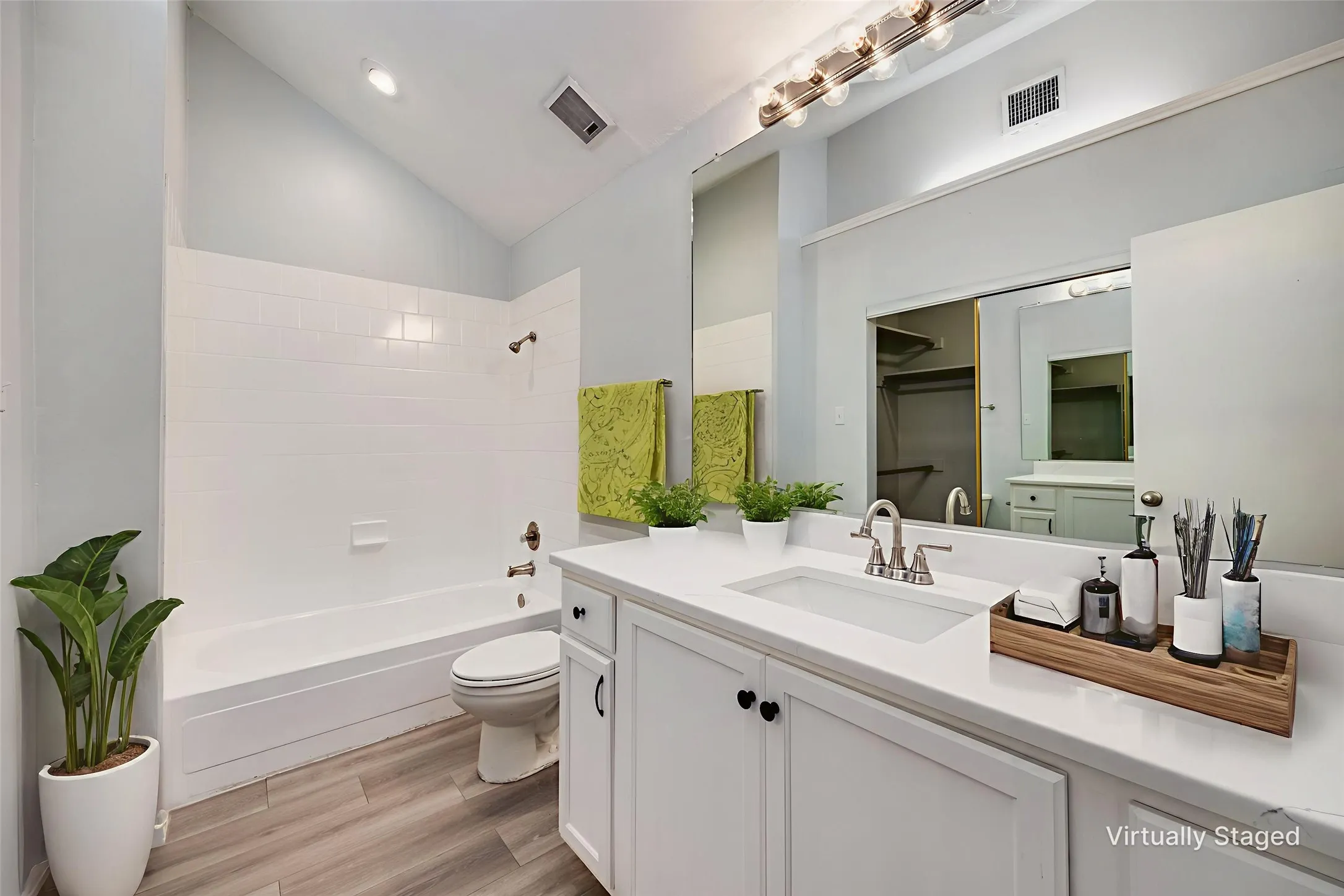 Bathroom featuring a white vanity with integrated sink, a large mirror, and a combination tub and shower
