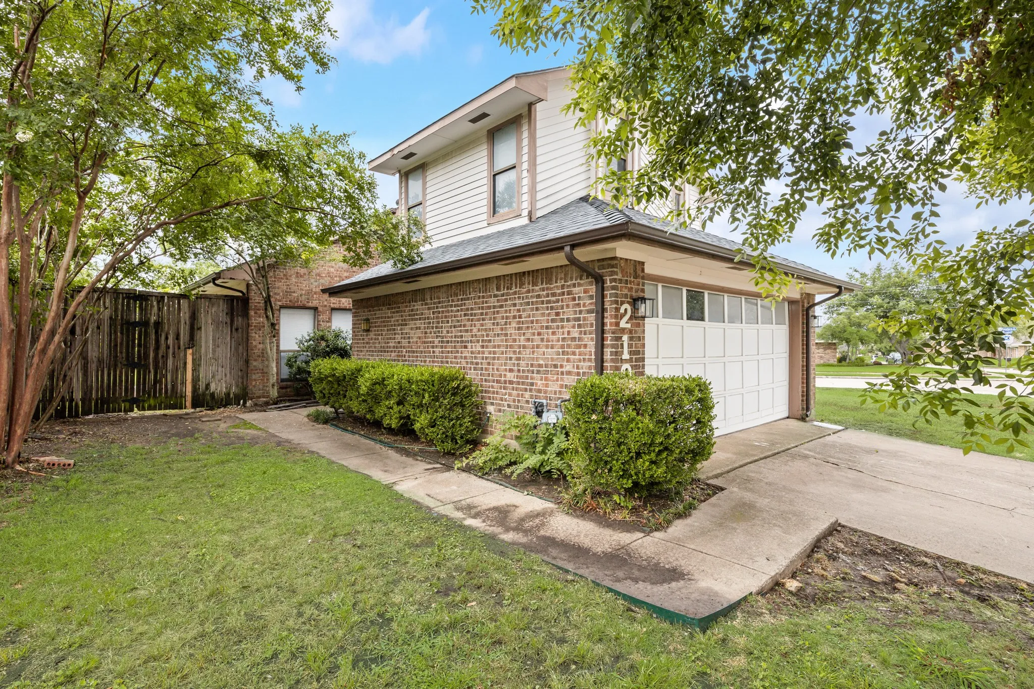 Brick and siding exterior featuring a white paneled garage door, concrete driveway, and mature landscaping
