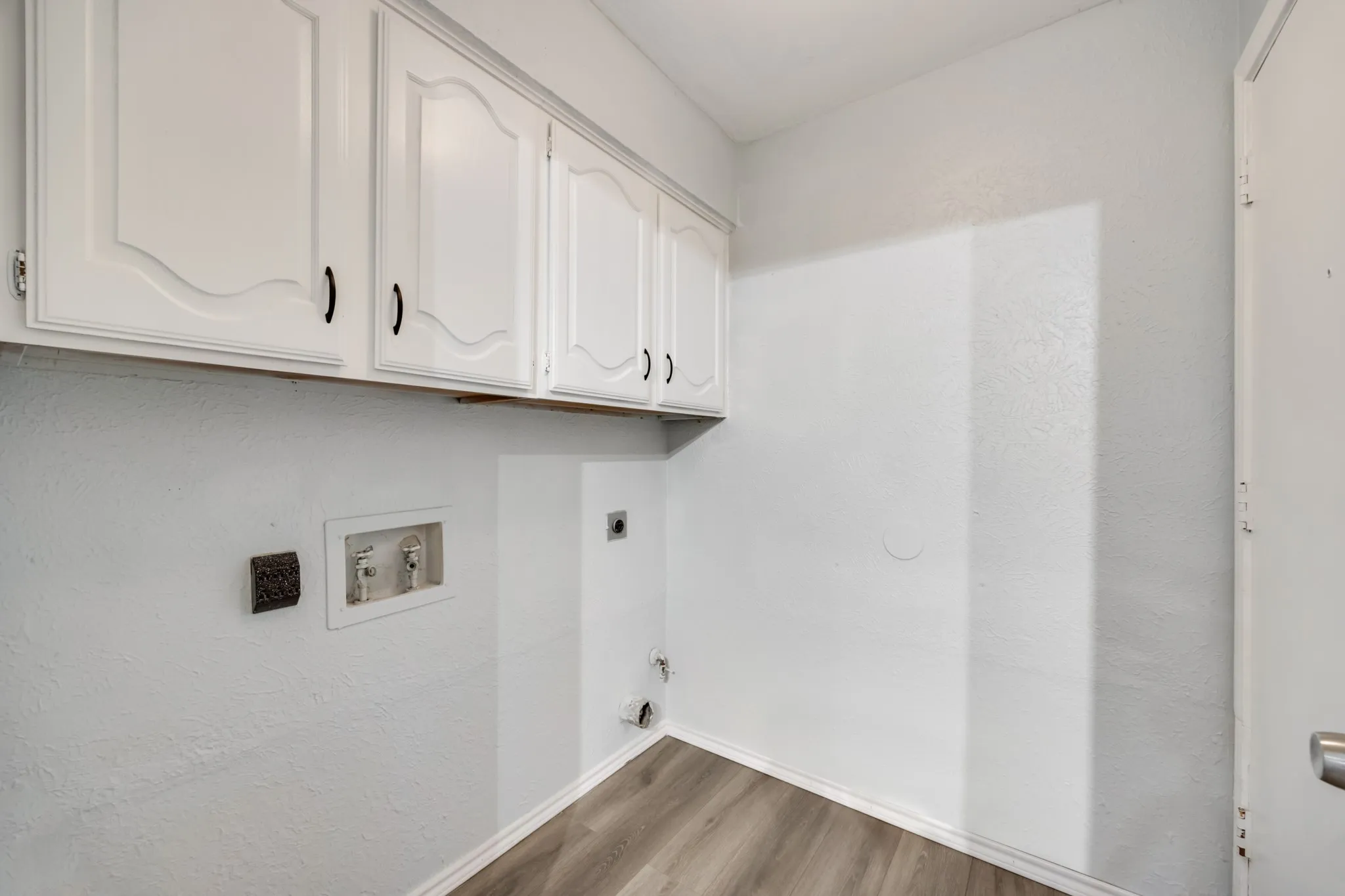 Dedicated laundry area featuring white wall cabinetry with black hardware, wood-finish flooring, and essential utility hookups