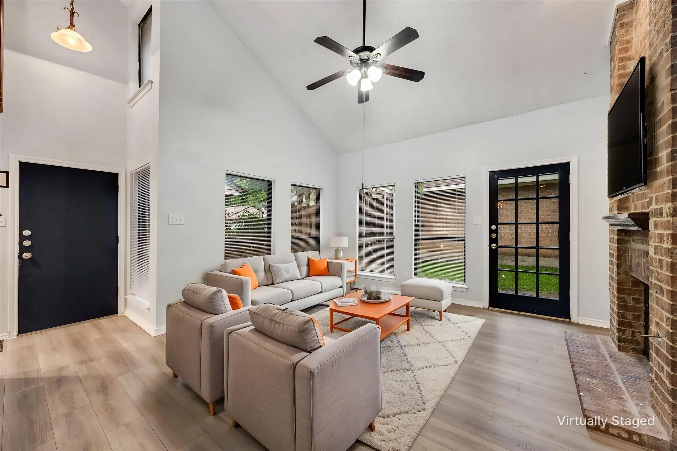 Vaulted ceiling living area featuring wood-finish flooring, a brick fireplace, and multiple windows