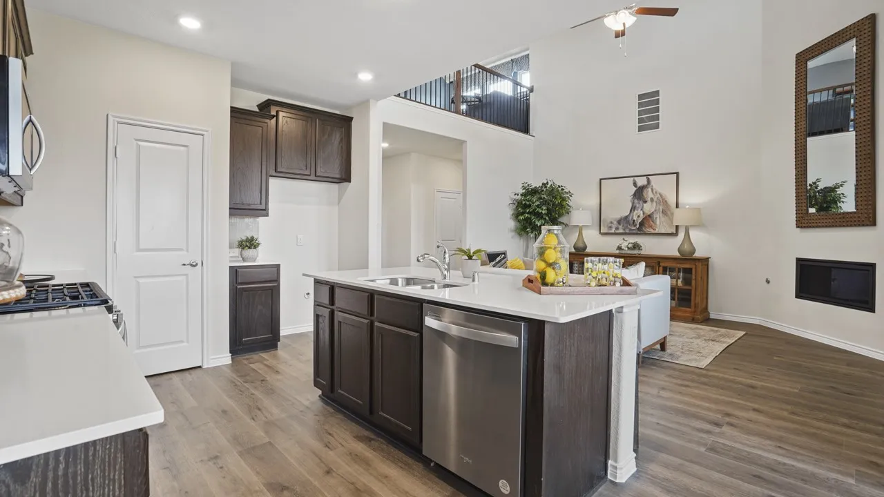 Open-concept kitchen featuring an island with integrated sink, stainless steel appliances, dark wood-finish cabinetry, light-toned countertops, and wood-finish flooring