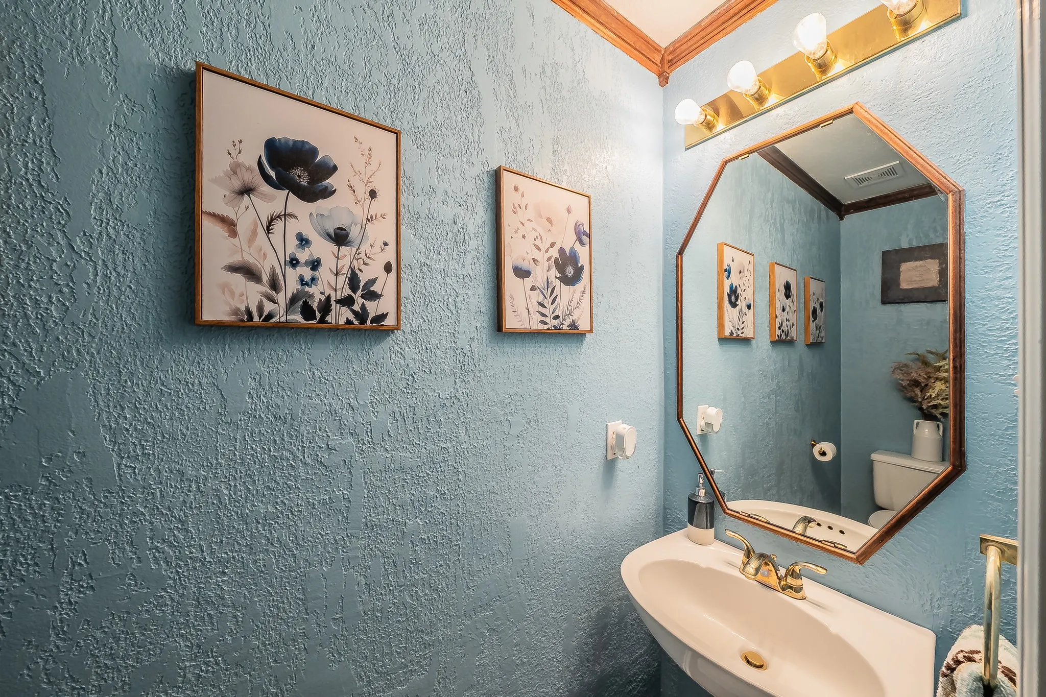 Pedestal sink with brass-finish faucet, an octagonal mirror, and overhead vanity lighting