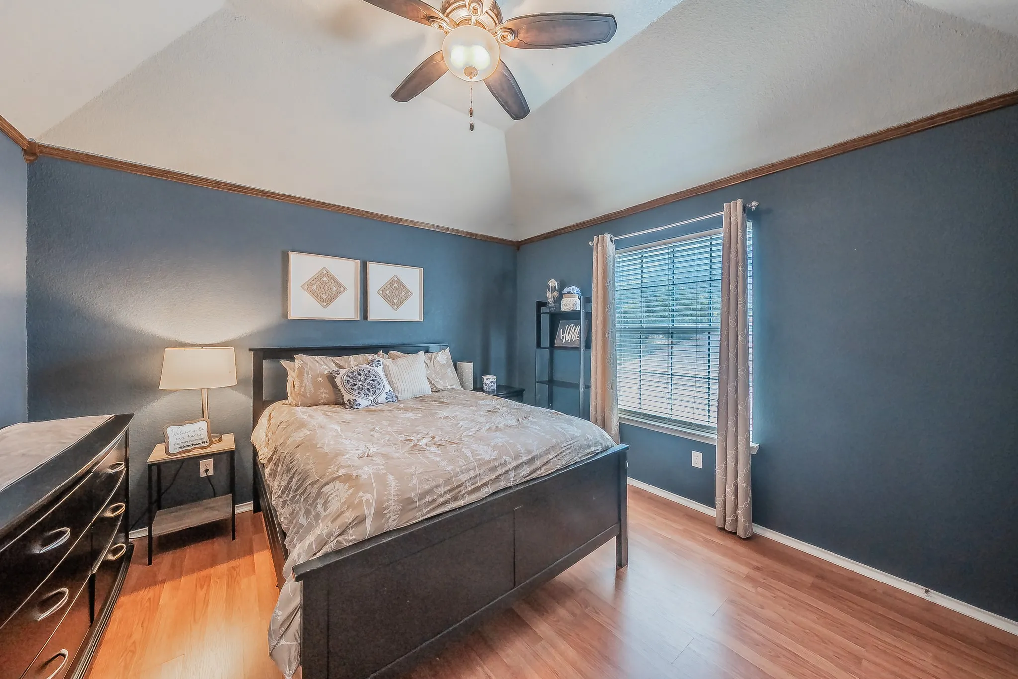 Vaulted ceilings featuring a ceiling fan, a window with blinds and curtains, and wood-finish flooring